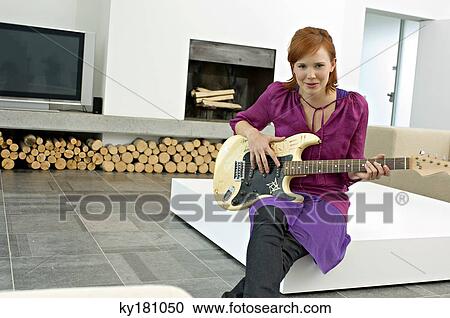 Portrait of a young woman sitting with a guitar on a coffee table and smiling View Large Photo Image Stock Image - Portrait of a young woman sitting with a guitar on a coffee table and smiling. Fotosearch