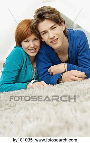 Stock Photography - Portrait of a young woman with a teenage boy lying on a carpet and smiling. Fotosearch