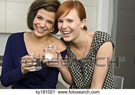 Stock Image - Portrait of two young women holding glasses of water and smiling. Fotosearch