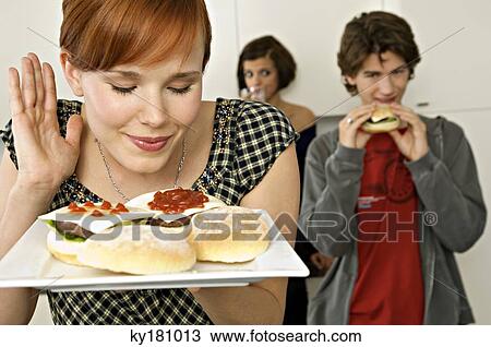 Stock Image - Young woman holding burgers in a tray with her friends in background. Fotosearch