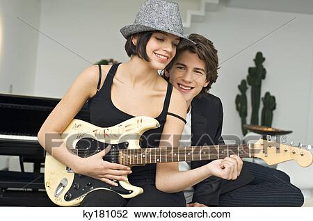 Young woman playing a guitar with a teenage boy leaning beside her View Large Photo Image Stock Image - Young woman playing a guitar with a teenage boy leaning beside her. Fotosearch