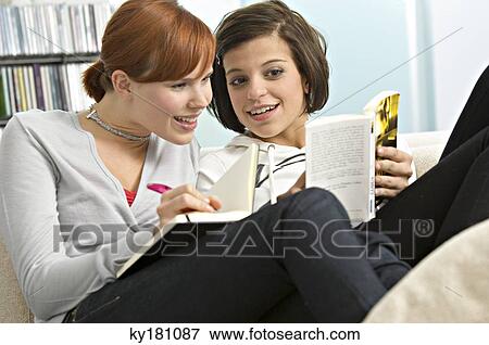 Young woman showing a book to her friend View Large Photo Image Stock Photo - Young woman showing a book to her friend. Fotosearch