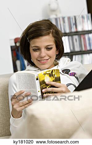 Young woman sitting on a couch and reading a book View Large Photo Image Stock Image - Young woman sitting on a couch and reading a book. Fotosearch