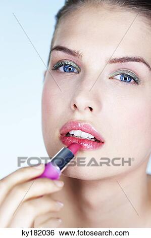 Portrait of young woman applying lipstick View Large Photo Image Stock Photograph - Portrait of young woman applying lipstick. Fotosearch
