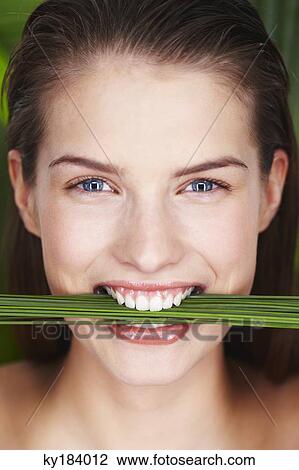 Stock Image - Young smiling woman holding plants between teeth. Fotosearch