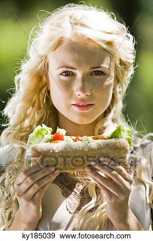 Portrait of a young blond woman holding a sandwich View Large Photo Image Stock Photo - Portrait of a young blond woman holding a sandwich. Fotosearch