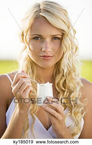Stock Photo - Portrait of young woman eating a yoghurt. Fotosearch