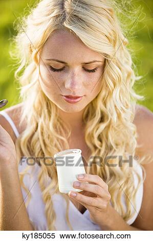 Stock Photography - Portrait of young woman eating a yoghurt. Fotosearch
