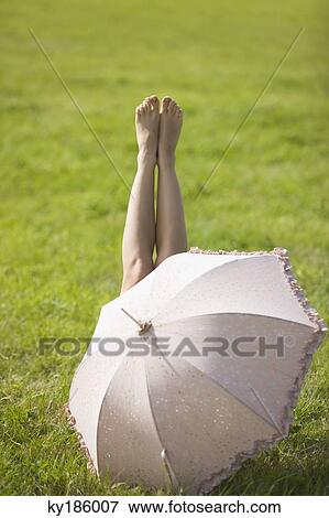 Young woman lying in grass, behind an umbrella View Large Photo Image Stock Photo - Young woman lying in grass, behind an umbrella. Fotosearch