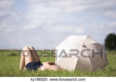 Young woman lying in grass, behind an umbrella View Large Photo Image Stock Photography - Young woman lying in grass, behind an umbrella. Fotosearch