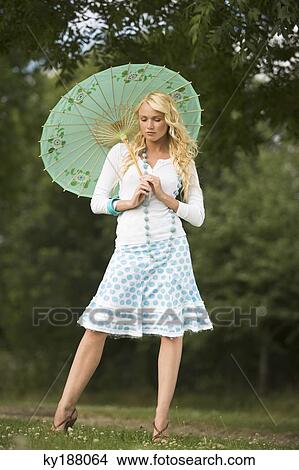 Young woman in a park, holding an umbrella View Large Photo Image Picture - Young woman in a park, holding an umbrella. Fotosearch