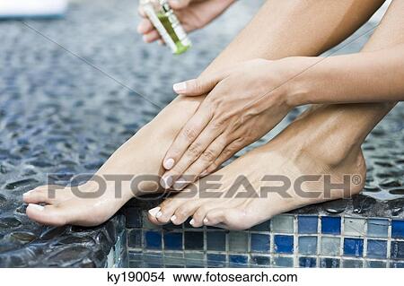 Picture - Woman applying oil on her legs at the poolside. Fotosearch