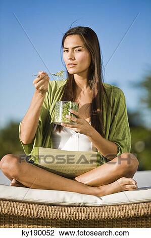 Stock Image - Woman sitting on a mattress and eating bean sprouts. Fotosearch