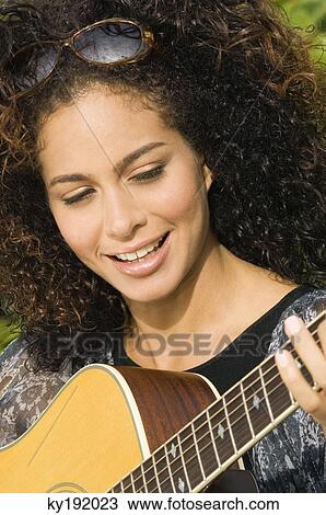Stock Image - Woman playing a guitar and smiling. Fotosearch