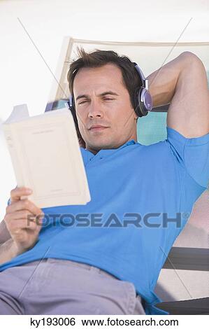 Man reading a book on a lounge chair View Large Photo Image Stock Photograph - Man reading a book on a lounge chair. Fotosearch