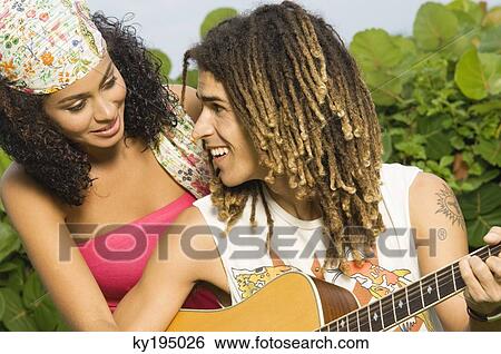 Stock Photograph - Couple playing a guitar and smiling at each other. Fotosearch