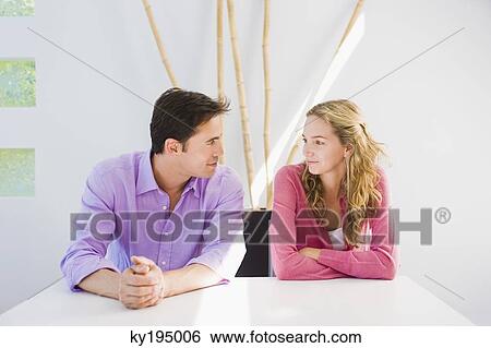 Couple sitting at a table and looking at each other View Large Photo Image Stock Photograph - Couple sitting at a table and looking at each other. Fotosearch