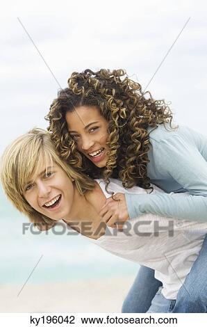 Stock Image - Girl riding piggyback on a teenage boy on the beach. Fotosearch