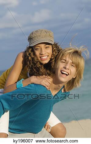 Girl riding piggyback on a teenage boy on the beach View Large Photo Image Stock Photo - Girl riding piggyback on a teenage boy on the beach. Fotosearch