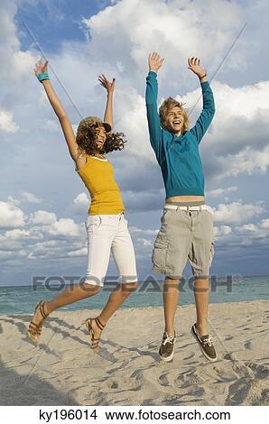 Teenage boy with a girl jumping on the beach View Large Photo Image Picture - Teenage boy with a girl jumping on the beach. Fotosearch