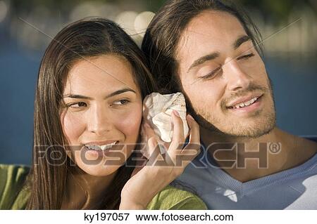 Couple listening to a shell View Large Photo Image Stock Photo - Couple listening to a shell. Fotosearch