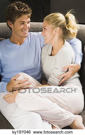 Couple sitting on a couch and smiling View Large Photo Image Stock Photograph - Couple sitting on a couch and smiling. Fotosearch