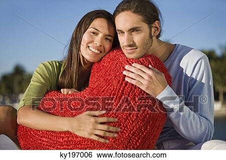 Portrait of a couple hugging a heart shaped cushion View Large Photo Image Stock Photograph - Portrait of a couple hugging a heart shaped cushion. Fotosearch