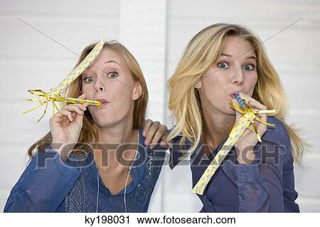 Stock Image - Two women blowing party horn blowers. Fotosearch