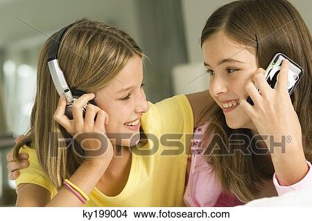 Girl talking on a mobile phone and her sister listening to headphones View Large Photo Image Picture - Girl talking on a mobile phone and her sister listening to headphones. Fotosearch