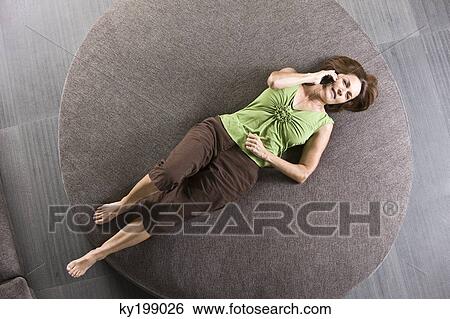 Woman lying on a round sofa and talking on a mobile phone View Large Photo Image Stock Photograph - Woman lying on a round sofa and talking on a mobile phone. Fotosearch