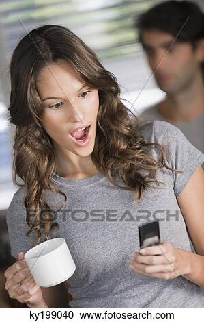 Woman text messaging on a mobile phone and looking surprised View Large Photo Image Stock Image - Woman text messaging on a mobile phone and looking surprised. Fotosearch