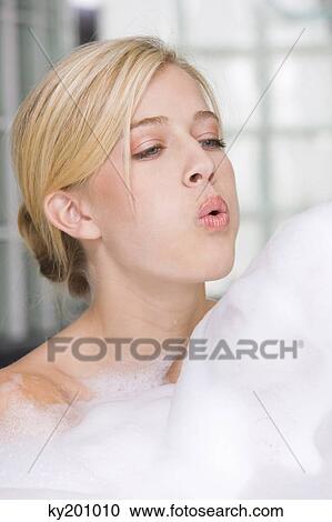 Stock Image - Woman blowing bubbles in a bathtub. Fotosearch