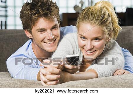 Couple holding a remote control and smiling View Large Photo Image Stock Image - Couple holding a remote control and smiling. Fotosearch