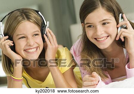 Girl talking on a mobile phone and her sister listening to headphones View Large Photo Image Stock Photo - Girl talking on a mobile phone and her sister listening to headphones. Fotosearch
