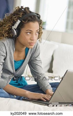 Girl working on a laptop and listening to headphones View Large Photo Image Stock Photo - Girl working on a laptop and listening to headphones. Fotosearch