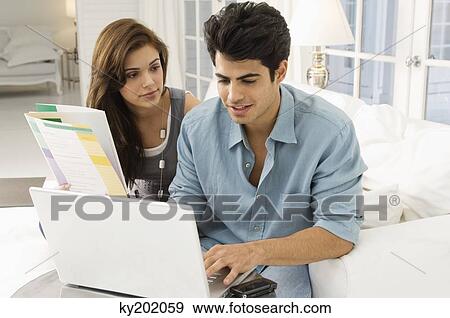 Man using a laptop with a woman sitting beside him View Large Photo Image Stock Photo - Man using a laptop with a woman sitting beside him. Fotosearch