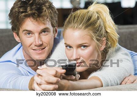 Portrait of a couple holding a remote control and smiling View Large Photo Image Stock Photo - Portrait of a couple holding a remote control and smiling. Fotosearch