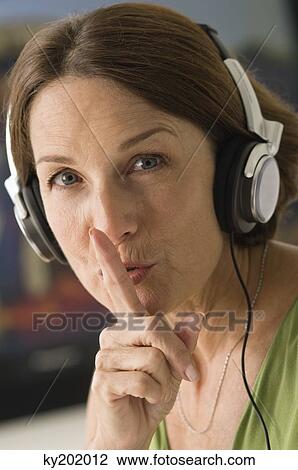 Stock Image - Woman listening to headphones with her finger on her lips. Fotosearch