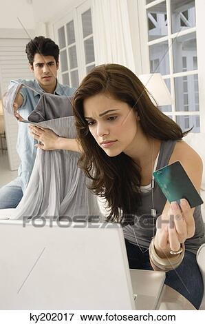 Woman shopping online with a credit card and her husband showing her a dress View Large Photo Image Stock Photo - Woman shopping online with a credit card and her husband showing her a dress. Fotosearch
