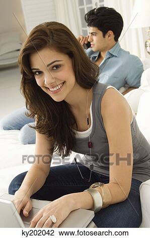Woman working on a laptop with a man talking on a mobile phone in the background View Large Photo Image Stock Image - Woman working on a laptop with a man talking on a mobile phone in the background. Fotosearch