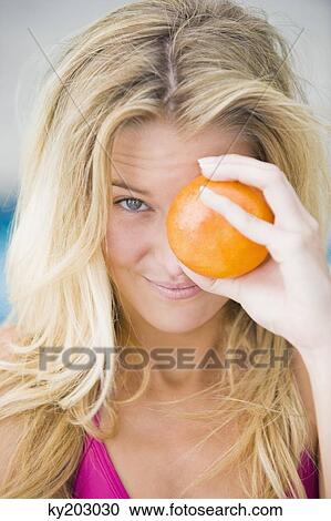 Close-up of a woman holding an orange in front of her eye View Large Photo Image Stock Image - Close-up of a woman holding an orange in front of her eye. Fotosearch
