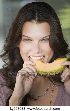Stock Photo - Portrait of a woman biting a slice of cantaloupe. Fotosearch