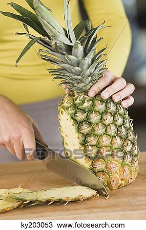 Stock Image - Woman cutting a pineapple. Fotosearch
