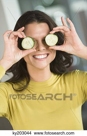 Woman holding cucumber slices in front of her eyes View Large Photo Image Picture - Woman holding cucumber slices in front of her eyes. Fotosearch