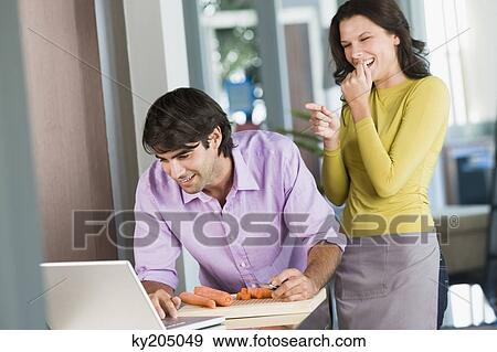 Man cooking with the recipe on a laptop and a woman laughing at him View Large Photo Image Stock Photo - Man cooking with the recipe on a laptop and a woman laughing at him. Fotosearch