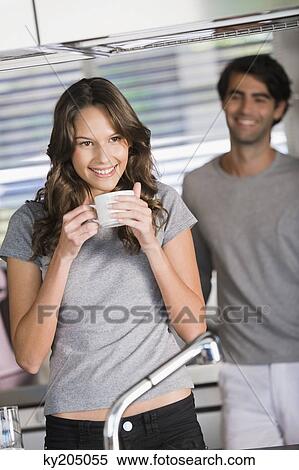 Woman drinking tea with a man standing in the background View Large Photo Image Stock Photography - Woman drinking tea with a man standing in the background. Fotosearch