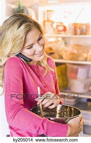 Woman holding a mixing bowl and talking on a mobile phone View Large Photo Image Picture - Woman holding a mixing bowl and talking on a mobile phone. Fotosearch