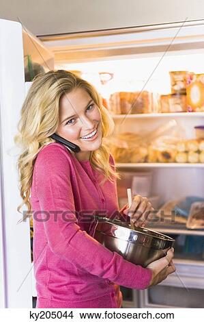 Woman holding a mixing bowl and talking on a mobile phone View Large Photo Image Picture - Woman holding a mixing bowl and talking on a mobile phone. Fotosearch