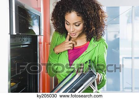 Stock Image - Woman looking into an oven in the kitchen. Fotosearch