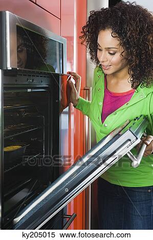 Stock Photography - Woman looking into an oven in the kitchen. Fotosearch